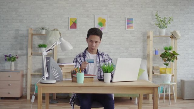 young asian man in a shirt enters data with a Bank card on a laptop