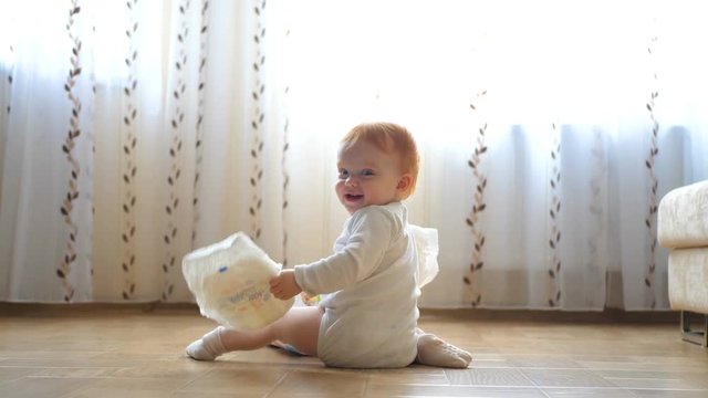 Redhead baby girl playing with diapers on the floor