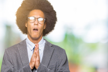 Young african american business man with afro hair wearing glasses begging and praying with hands...