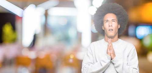 Young african american man with afro hair wearing sporty sweatshirt begging and praying with hands together with hope expression on face very emotional and worried. Asking for forgiveness. 