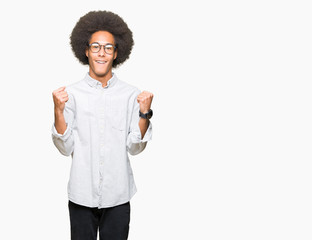 Young african american man with afro hair wearing glasses celebrating surprised and amazed for success with arms raised and open eyes. Winner concept.