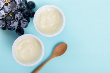 Two plastic cups of yoghurt with wooden spoon and grape on pastel background, healthy eating, top view