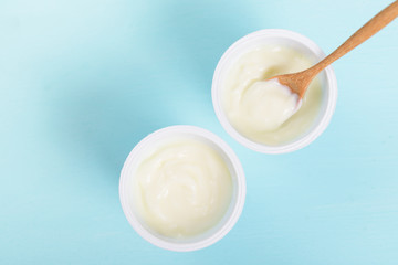 Plastic cup of yoghurt with wooden spoon on pastel background, healthy eating, top view