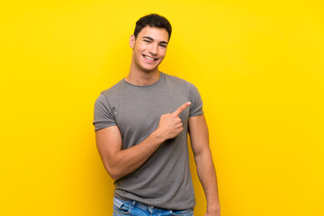 Handsome man over isolated yellow wall pointing to the side to present a product