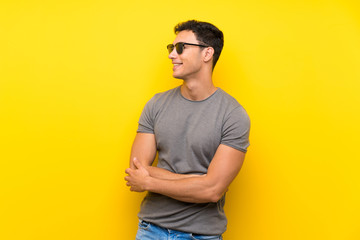 Handsome man over isolated yellow wall with glasses and happy