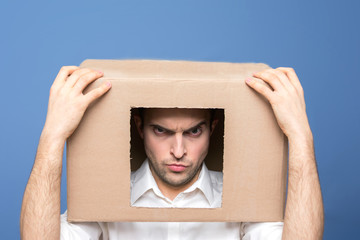 Angry man with box on head, front view, emotions concept human, blue background