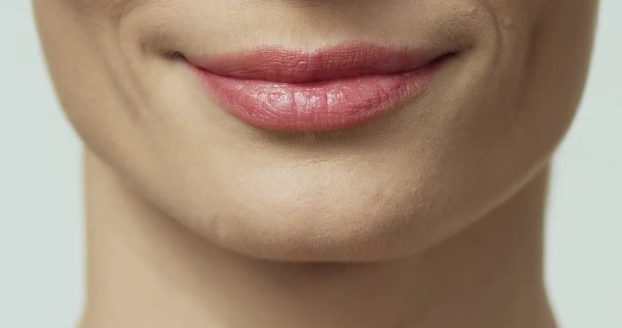 Close up of the mouth of the Caucasian female lips with a pink gloss while she smiling on the white wall background.