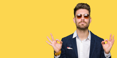 Young handsome elegant man wearing sunglasses and fashion blazer relax and smiling with eyes closed doing meditation gesture with fingers. Yoga concept.