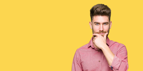 Young handsome business casual man looking confident at the camera with smile with crossed arms and hand raised on chin. Thinking positive.