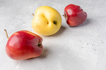 Three ugly red and yellow apples are lying chaotically on grey concrete background.