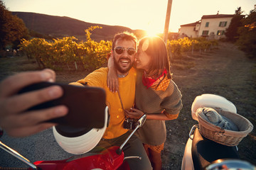 Man and woman on romantic journey on scooter at sunset and take selfie..