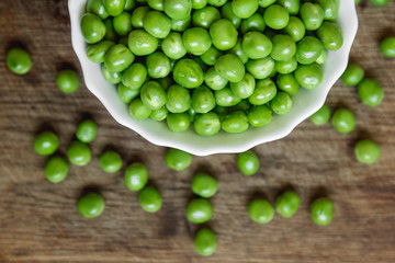 Fresh green peas in a white plate on wooden background, top view. Rustic table background