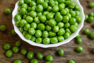 Fresh green peas in a white plate on wooden background, top view. Rustic table background