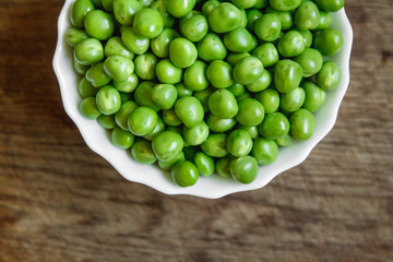 Fresh green peas in a white plate on wooden background, top view. Rustic table background