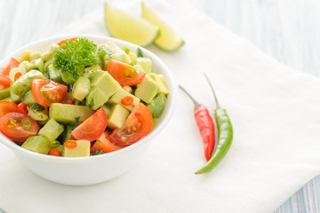 Salsa from avocado, cherry tomatoes and lime. Traditional salad from fresh vegetables with avocado. A serving is serialized in a deep white bowl on a white napkin. Close up and horizontal orientation.