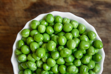 Fresh green peas in a white plate on wooden background, top view. Rustic table background