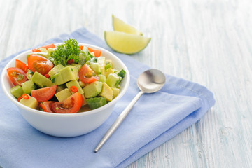 Salsa from avocado, cherry tomatoes and lime. Traditional salad from fresh vegetables with avocado. A serving is serialized in a deep white bowl on a blue napkin. Space for text. 