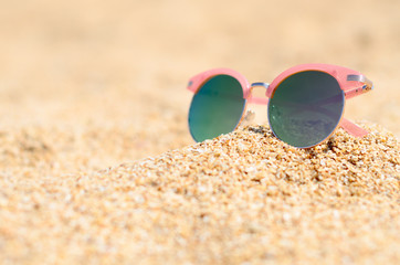 Fototapeta na wymiar Pink sunglasses against the sun on the beach sand