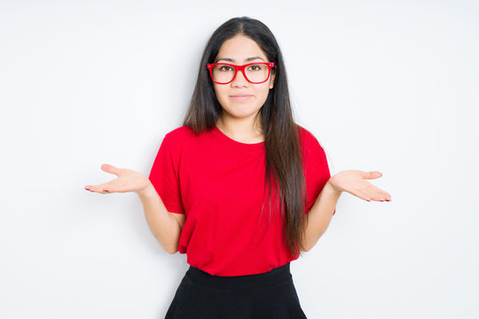 Beautiful brunette woman wearing red glasses over isolated background clueless and confused expression with arms and hands raised. Doubt concept.