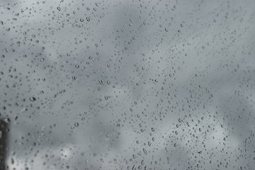 Rain water drops on the window glass, blurred background of clouds on the sky