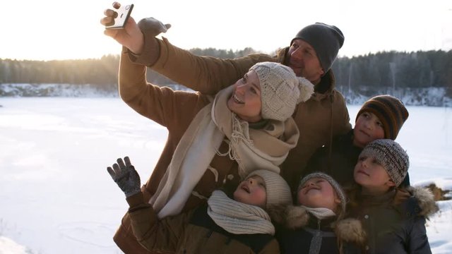 Close-up shot of cheerful young family huddled together and taking selfies on smartphone with enthusiasm and excitement, mom helping dad to adjust frame, then admiring their photos