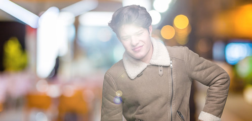 Naklejka premium Young handsome man wearing winter coat over isolated background Suffering of backache, touching back with hand, muscular pain
