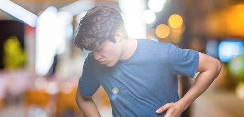 Young handsome man wearing blue t-shirt over isolated background with hand on stomach because nausea, painful disease feeling unwell. Ache concept.