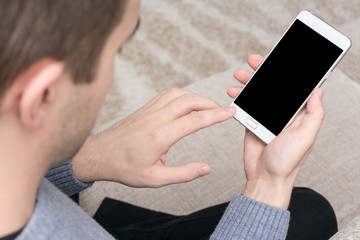 Man uses smart phone, sitting at home on the couch, touch screen, men's hand, close up, copy space