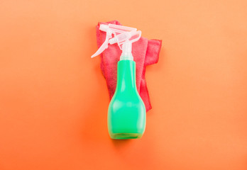 Green spray bottle for cleaning on pink microfiber cloth on orange background. Minimal cleaning concept