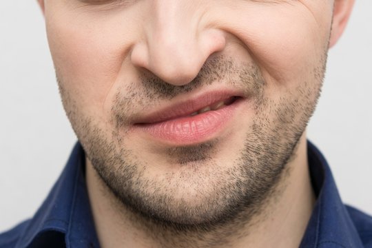 Grimace of irritation or discontent on the face of a bearded male, close up, cropped image