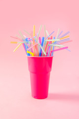multicolored plastic cocktail straws in plastic cup on a pink background. Concept: holiday, party, ecology, plastic