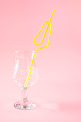 yellow plastic pear shaped cocktail straw in glass on pink background. Concept holiday