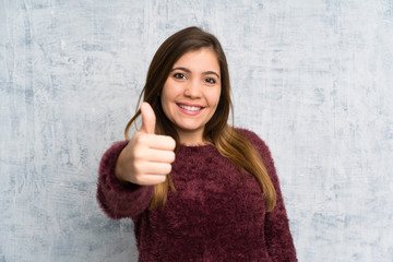 Young girl over grunge wall giving a thumbs up gesture