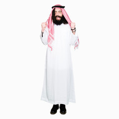 Arabian business man with long hair wearing traditional keffiyeh scarf excited for success with arms raised celebrating victory smiling. Winner concept.