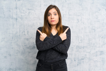 Young girl over grunge wall pointing to the laterals having doubts