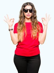 Obraz na płótnie Canvas Young beautiful woman wearing red t-shirt and sunglasses relax and smiling with eyes closed doing meditation gesture with fingers. Yoga concept.