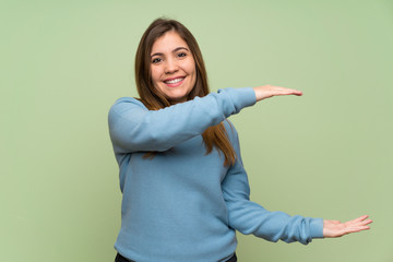 Young girl over green wall holding copyspace to insert an ad