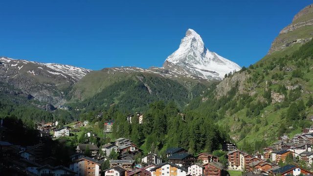 Aerial view of Matterhorn mountain at turn of spring and summer, snowy peaks and lush green valley, Zermatt town in foreground - landscape panorama of Swiss Alps from above, Switzerland, Europe