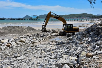 Crawler excavator are moving rocks to make breakwater on the beach. The beach , mountains and blue...