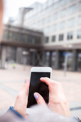 Businesswoman uses a mobile phone on the street against an office building.