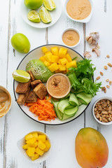 Healthy summer fresh salad with mango, avocado, lime and tofu with sweet peanut butter dressing on white wooden table