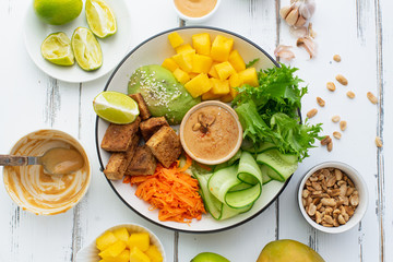 Healthy summer fresh salad with mango, avocado, lime and tofu with sweet peanut butter dressing on white wooden table