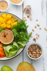 Healthy summer fresh salad with mango, avocado, lime and tofu with sweet peanut butter dressing on white wooden table