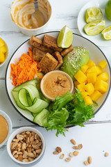Healthy summer fresh salad with mango, avocado, lime and tofu with sweet peanut butter dressing on white wooden table