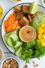 Healthy summer fresh salad with mango, avocado, lime and tofu with sweet peanut butter dressing on white wooden table