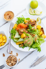 Healthy summer fresh salad with mango, avocado, lime and tofu with sweet peanut butter dressing on white wooden table