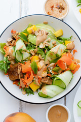 Healthy summer fresh salad with mango, avocado, lime and tofu with sweet peanut butter dressing on white wooden table