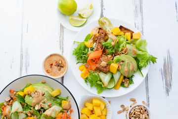 Healthy summer fresh salad with mango, avocado, lime and tofu with sweet peanut butter dressing on white wooden table