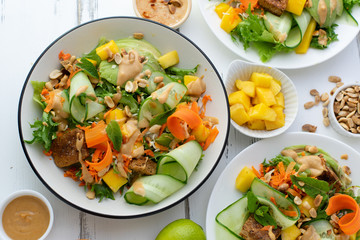 Healthy summer fresh salad with mango, avocado, lime and tofu with sweet peanut butter dressing on white wooden table