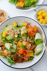 Healthy summer fresh salad with mango, avocado, lime and tofu with sweet peanut butter dressing on white wooden table
